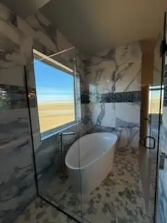 Modern bathroom featuring a freestanding tub, glass shower enclosure, and elegant marble walls with a scenic view outsides
